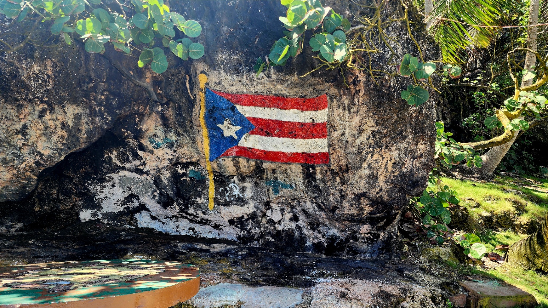Puerto Rican flag painted on a weathered rock wall surrounded by tropical greenery
