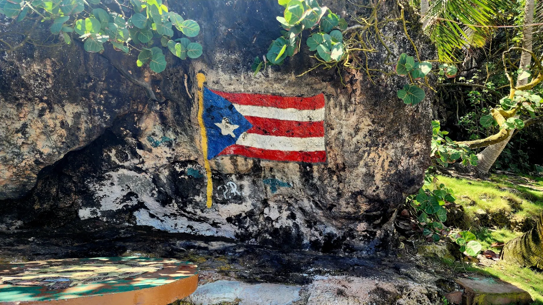 Puerto Rican flag painted on a weathered rock wall surrounded by tropical greenery